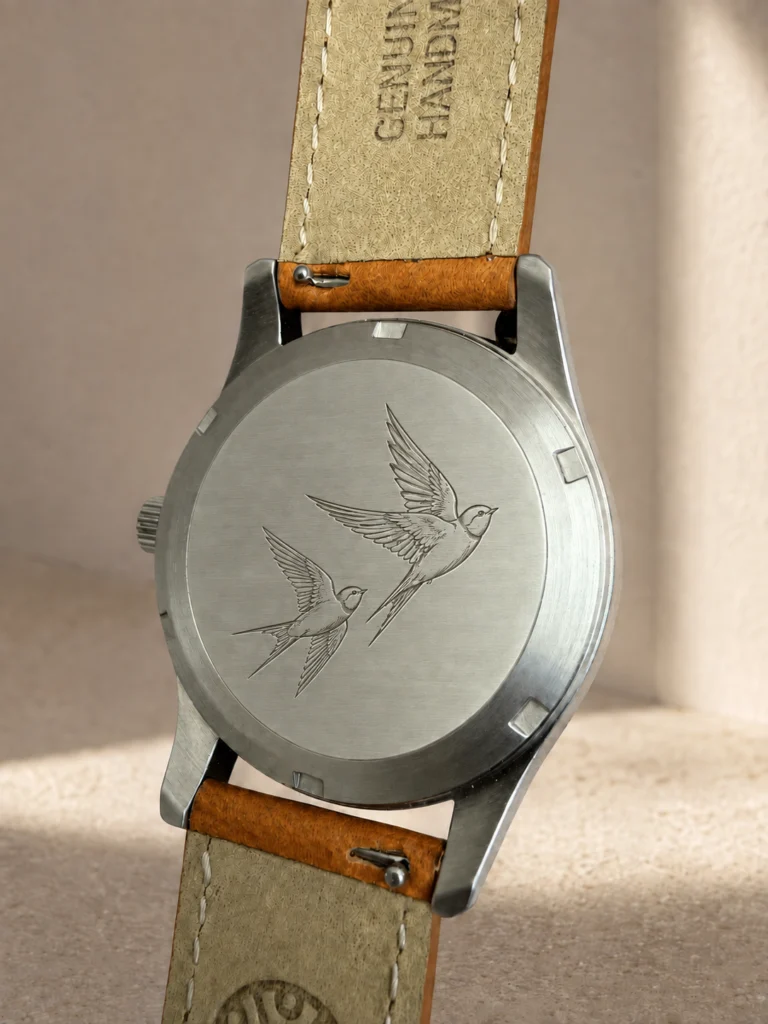 Solid steel Knez caseback engraved with two swallows in flight, on a cognac leather strap.